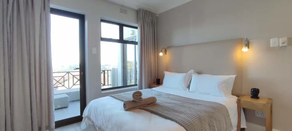 Modern bedroom with white bedding, deck access, and garden views