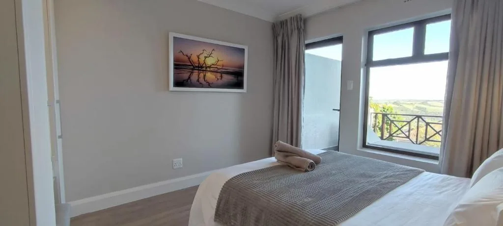 Modern bedroom with bed, landscape artwork, and scenic balcony views