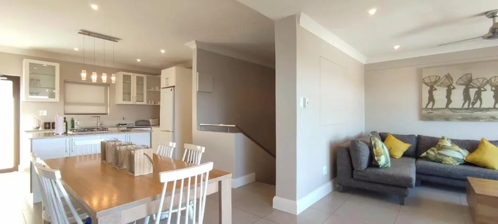 Open-plan dining area with wooden table and white chairs, kitchen visible beyond
