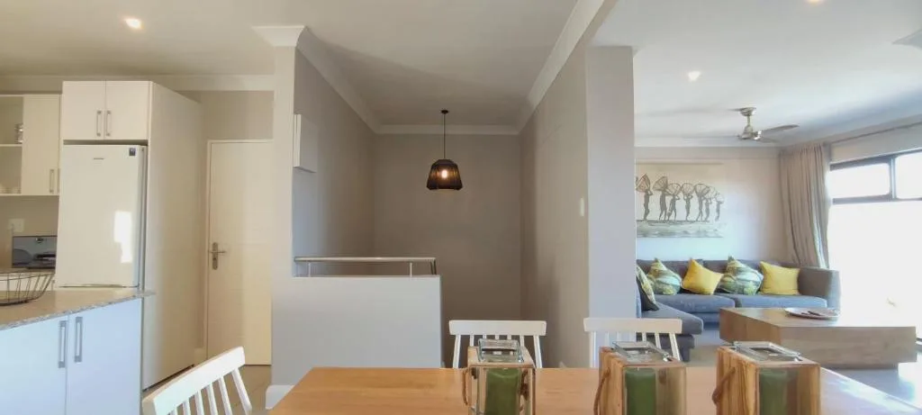 Open-plan dining area with wooden table and white chairs, kitchen visible beyond