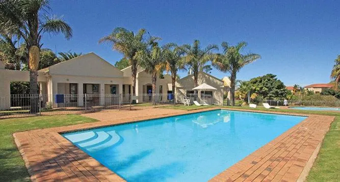 Large rectangular swimming pool with brick patio and palm-lined grounds
