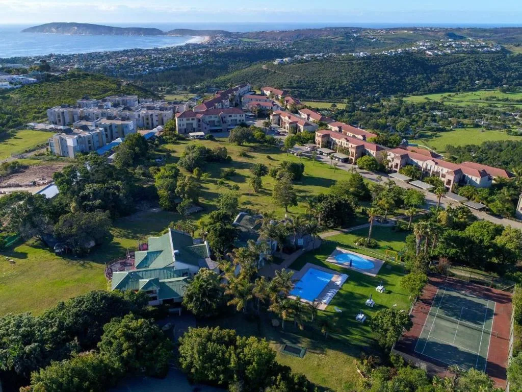Aerial view of property with pool, gardens, and coastline beyond