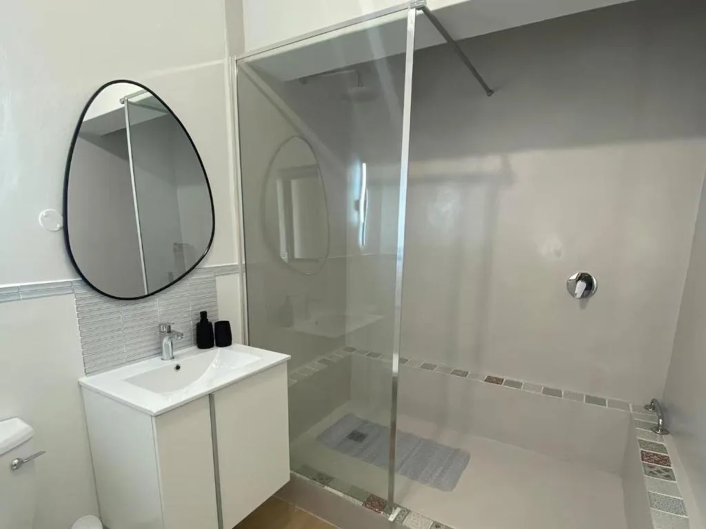 Modern bathroom with vanity sink, round mirror, and glass shower enclosure