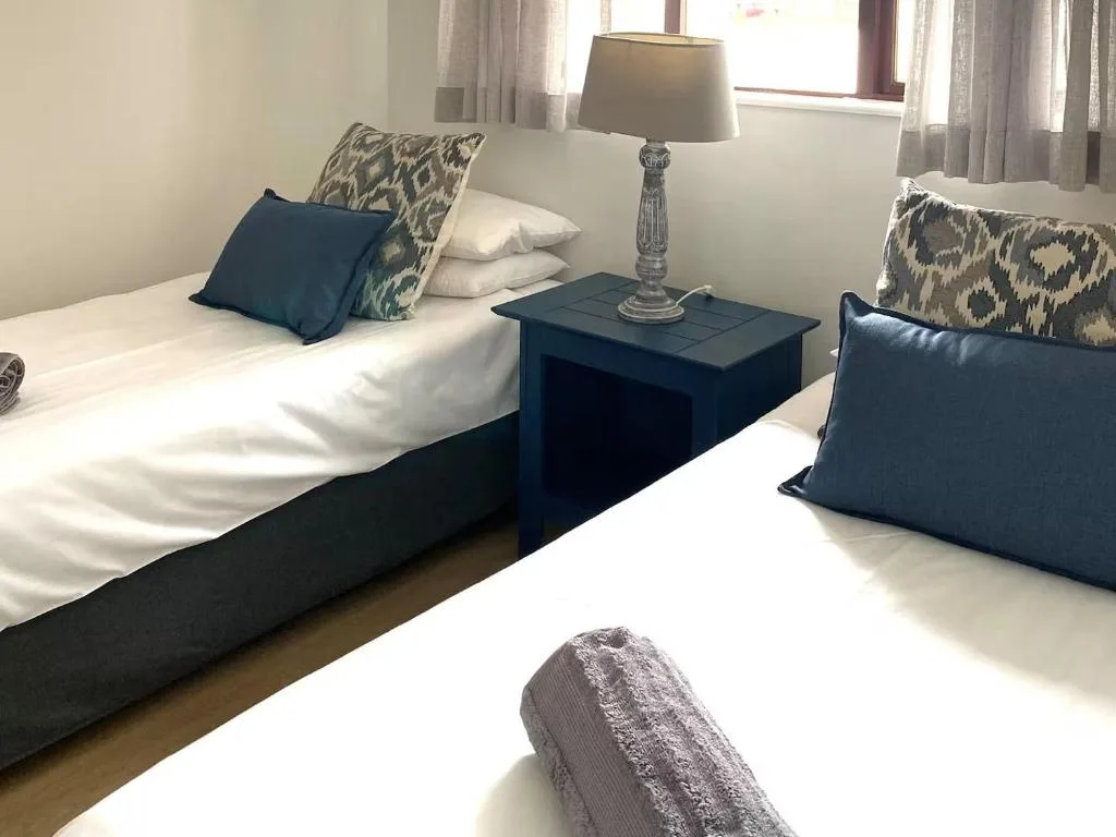 Twin beds with navy pillows and patterned cushions, bedside lamp and table