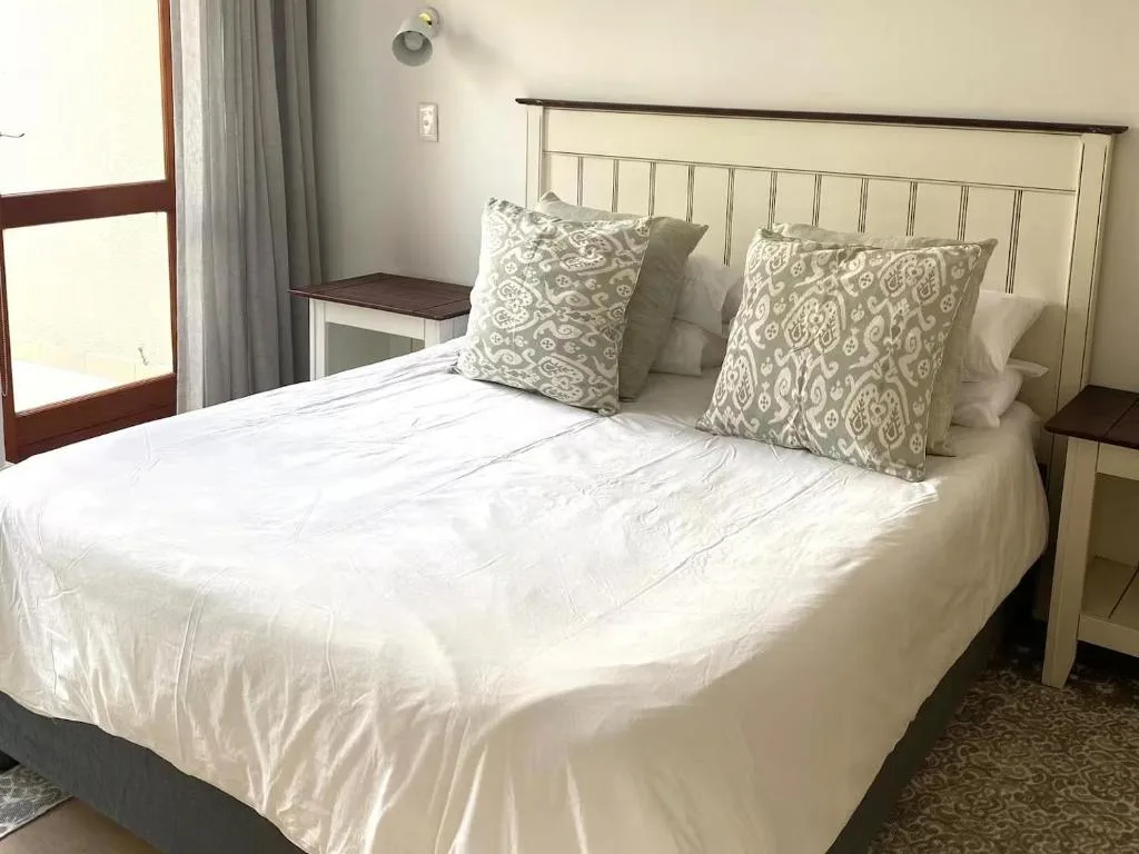 Bright bedroom with white bedding and patterned cushions, cream headboard