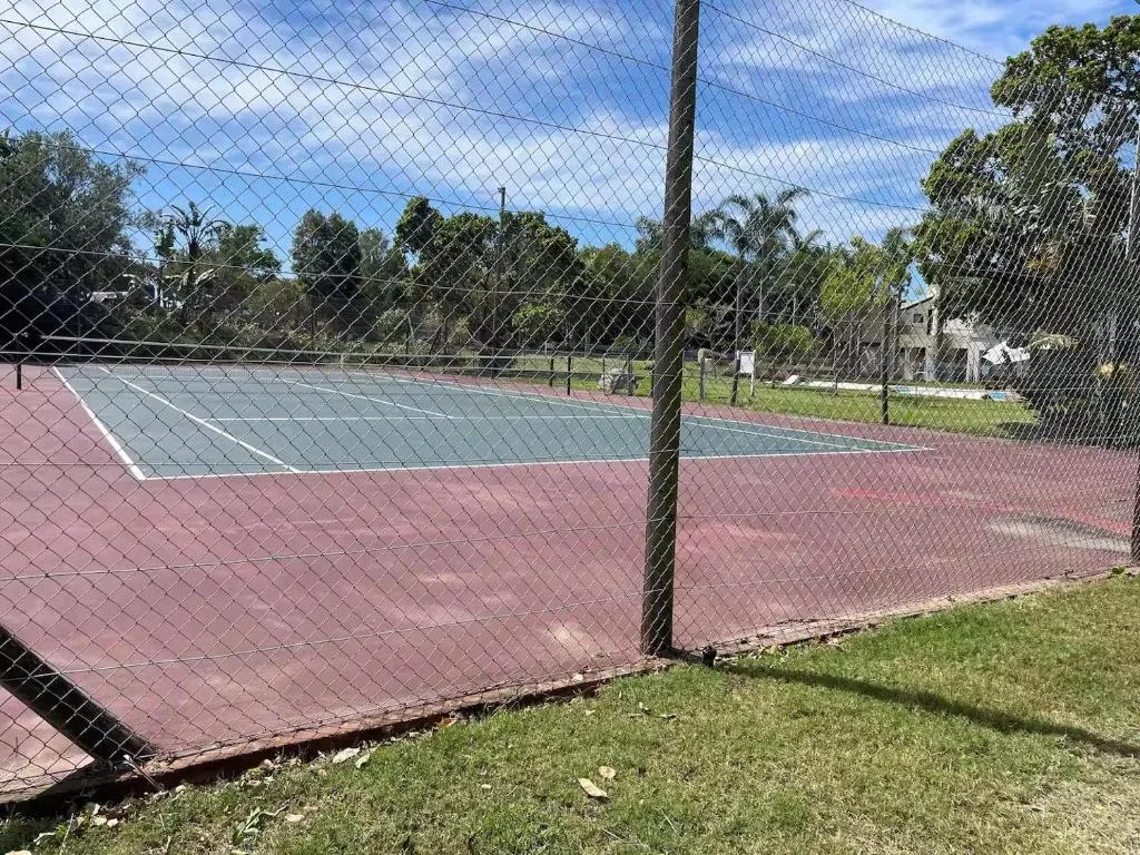 Tennis court with red and blue surface behind chain-link fence