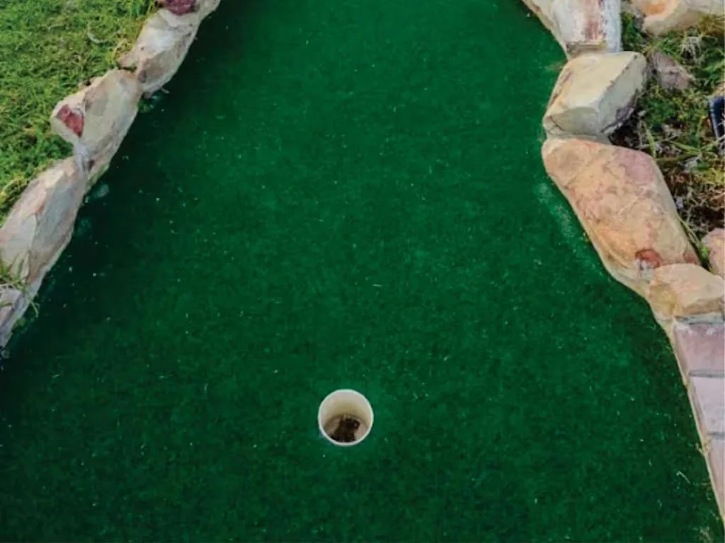 Miniature golf hole with green turf and stone borders