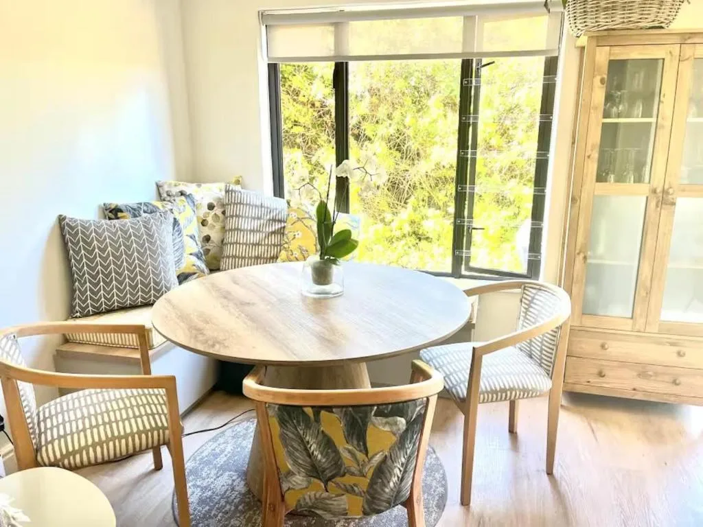Bright dining area with round wooden table and woven chairs overlooking garden