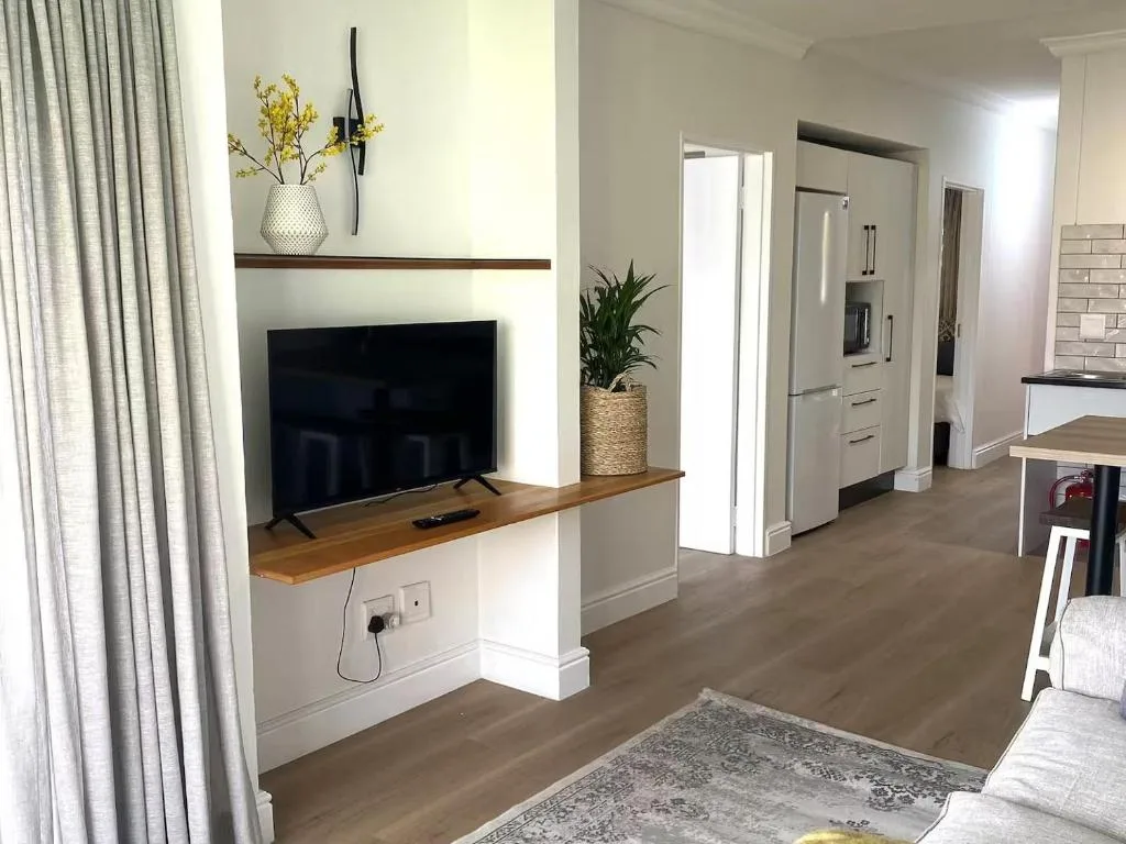 Modern living room with wall-mounted TV, wooden shelf, and kitchen visible beyond