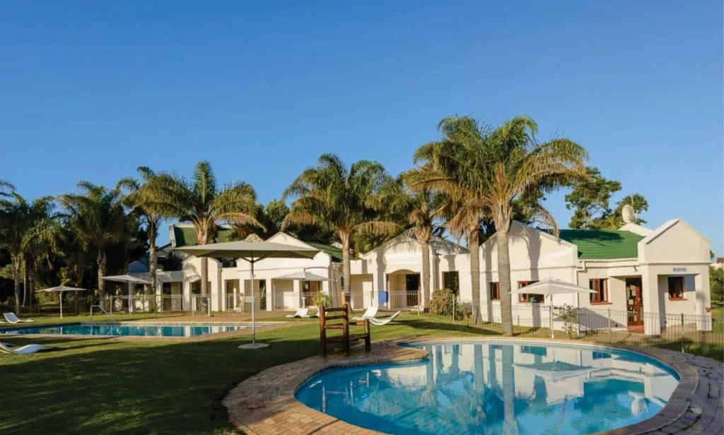 Two swimming pools with white buildings and palm trees in background