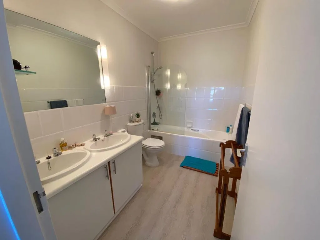 Modern bathroom with dual vanity, toilet, and glass-enclosed shower tub