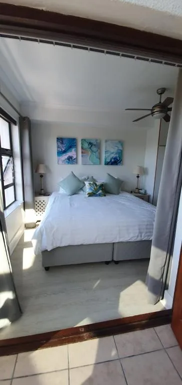 Bright bedroom with white bedding, blue artwork, and ceiling fan