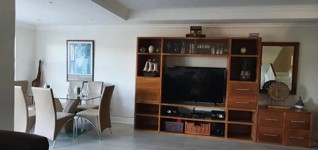 Modern lounge with wooden entertainment unit and dining area visible