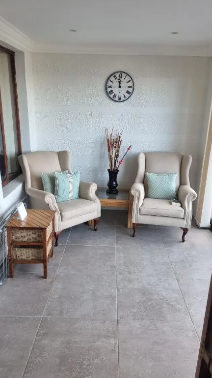 Bright lounge with two cream armchairs and wall clock decor