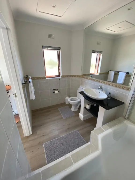 Modern bathroom with white vanity, toilet, and two windows with natural light