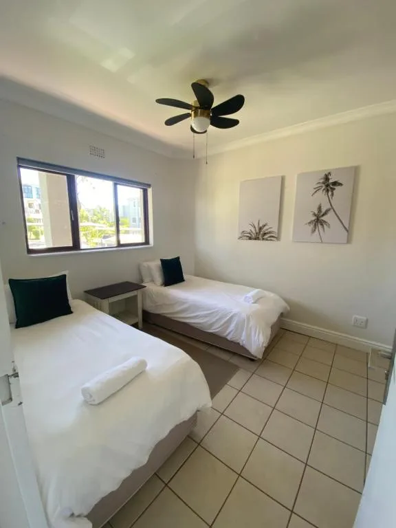 Bright twin bedroom with two single beds, ceiling fan, and palm artwork