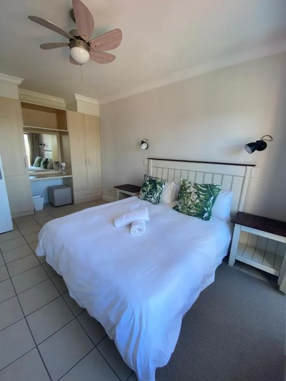 Bright bedroom with double bed, decorative pillows, ceiling fan, and vanity mirror