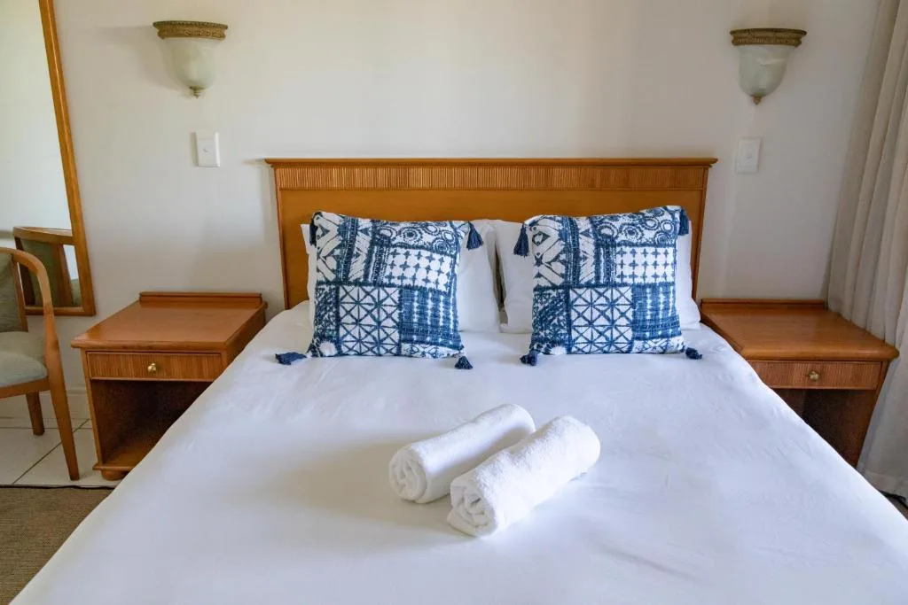 Spacious bedroom with wooden bed frame, blue patterned pillows, rolled towels