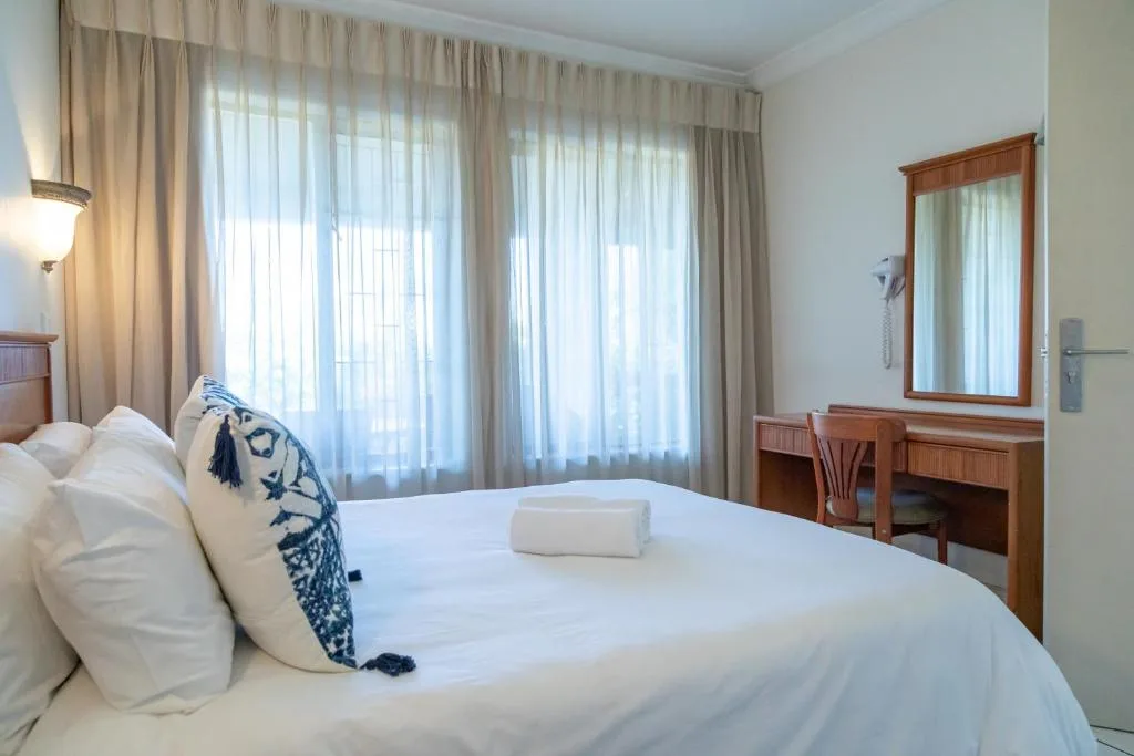 Bright bedroom with white bedding, wooden desk, and sheer curtains