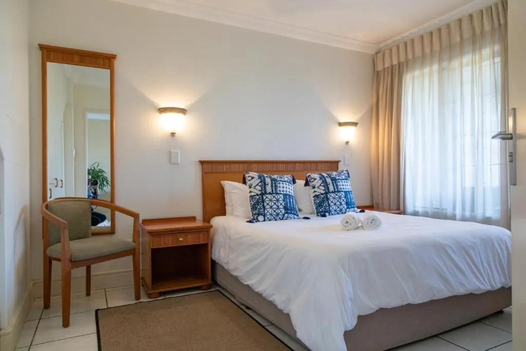 Bright bedroom with queen bed, wooden headboard, blue patterned pillows, and sheer curtains