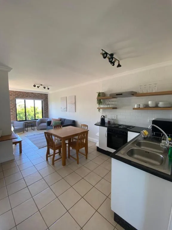 Open-plan kitchen with dining area and lounge visible beyond brick feature wall