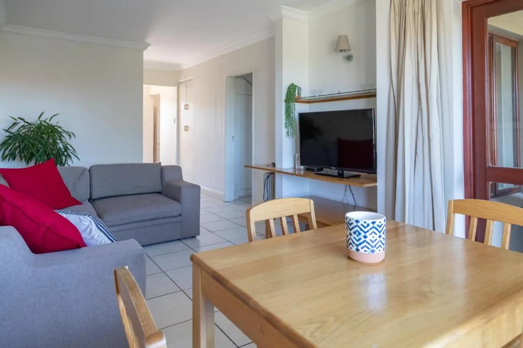 Open-plan lounge and dining area with gray sofa, wooden dining table, and TV