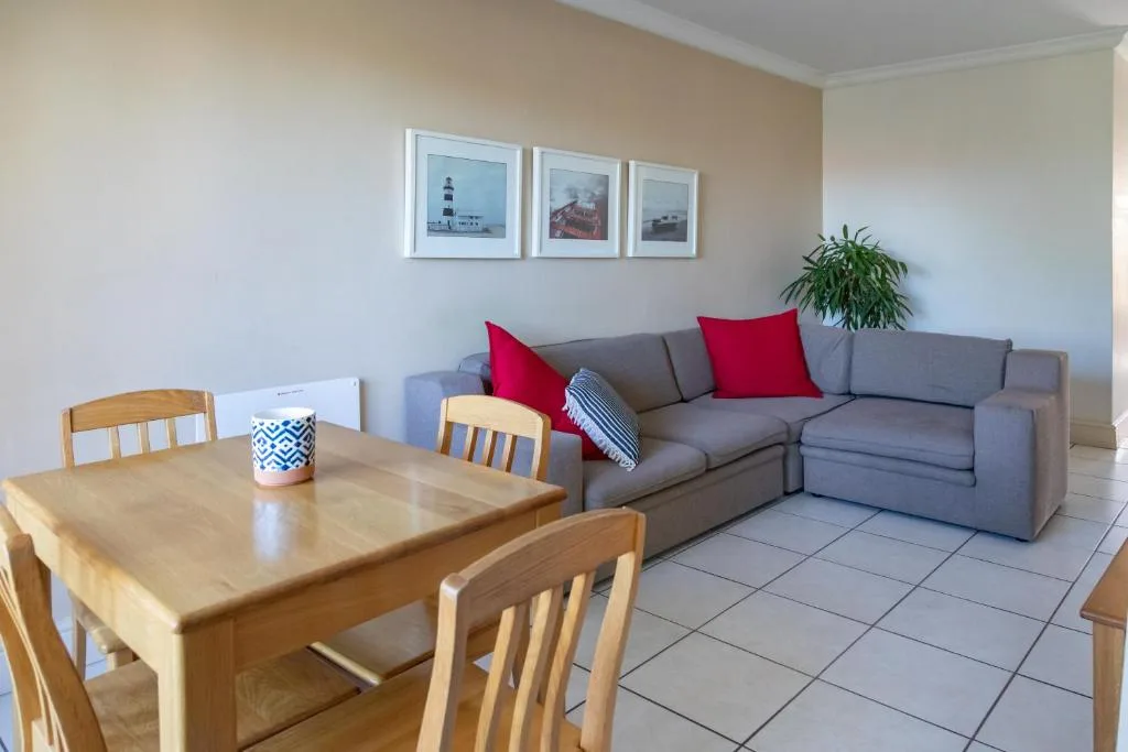 Bright living room with gray sofa, red cushions, wooden dining table, framed coastal artwork