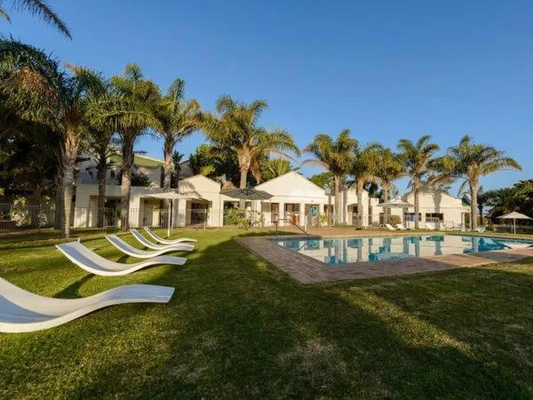 Swimming pool with loungers and white villa architecture surrounded by palm trees