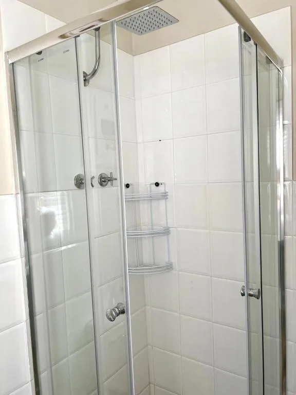 Modern glass shower enclosure with overhead rainfall showerhead and white tile surround