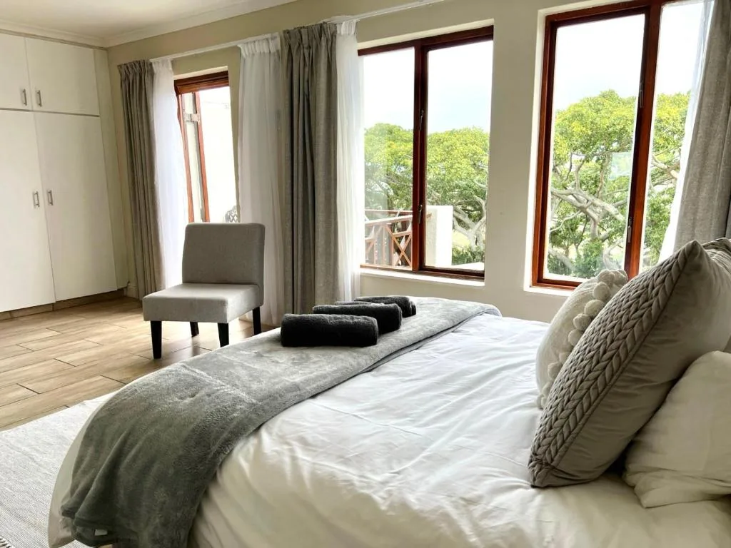 Bright bedroom with large bed, armchair, and tree views through glass doors