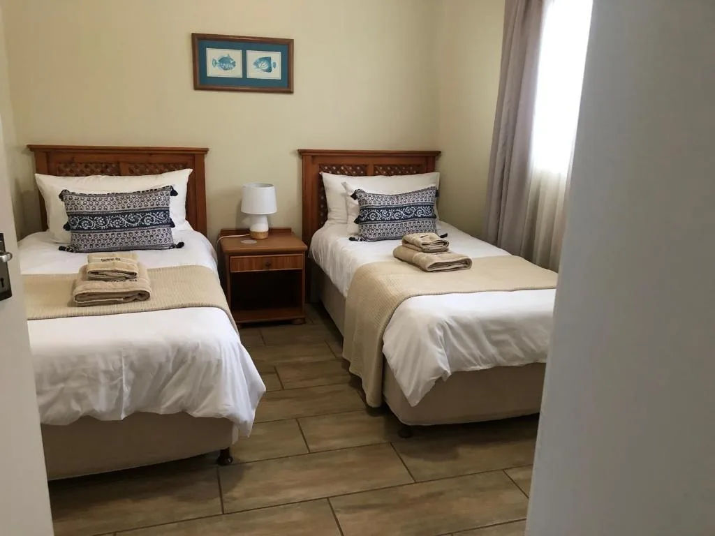 Twin bedroom with wooden beds, white linens, decorative pillows, and bedside table