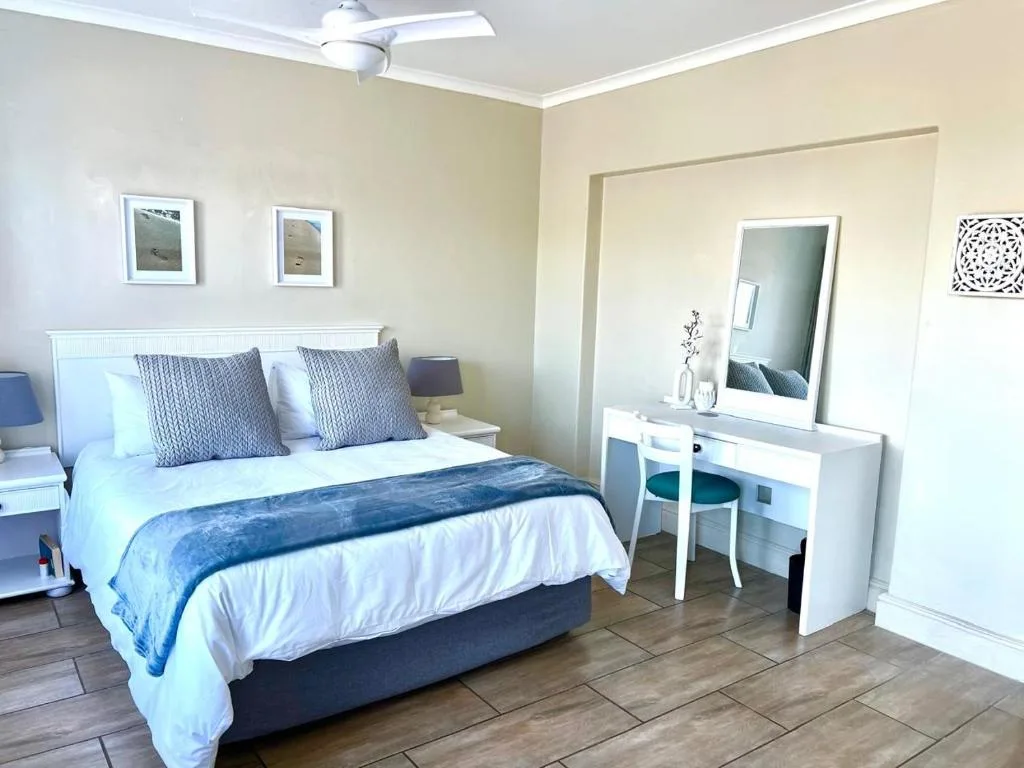 Bright bedroom with queen bed, decorative pillows, vanity mirror, and ceiling fan