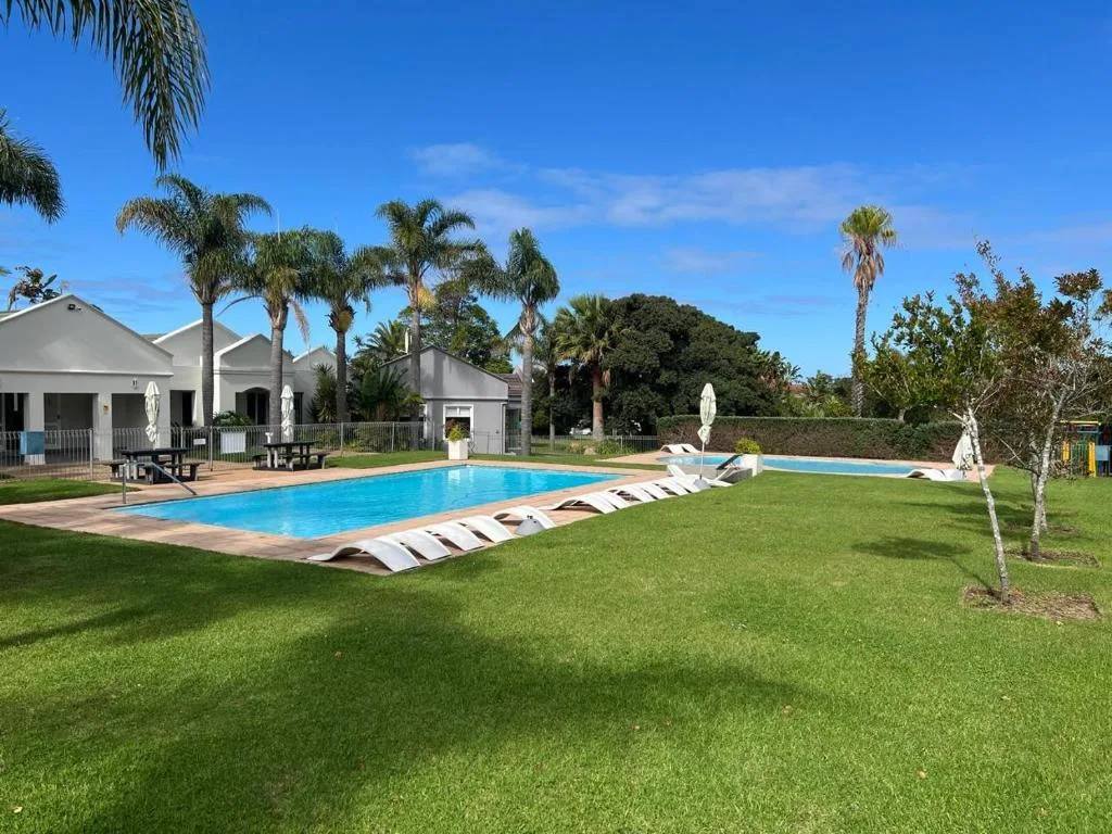 Resort swimming pool with loungers and white buildings on spacious green grounds