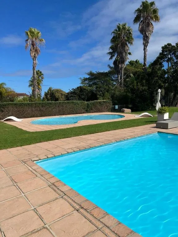 Two bright blue swimming pools with terracotta paving and manicured garden