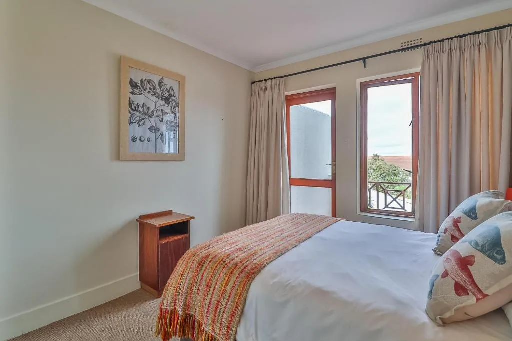 Bright bedroom with double bed, wooden nightstand, framed wall art, and balcony doors