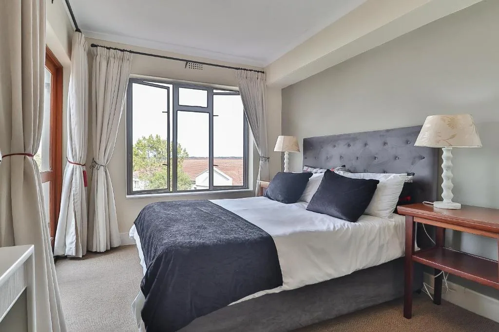 Spacious bedroom with queen bed, grey headboard, and large windows overlooking garden