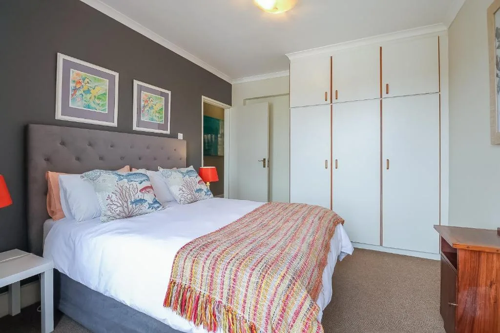 Spacious bedroom with queen bed, white built-in wardrobes, and colorful artwork