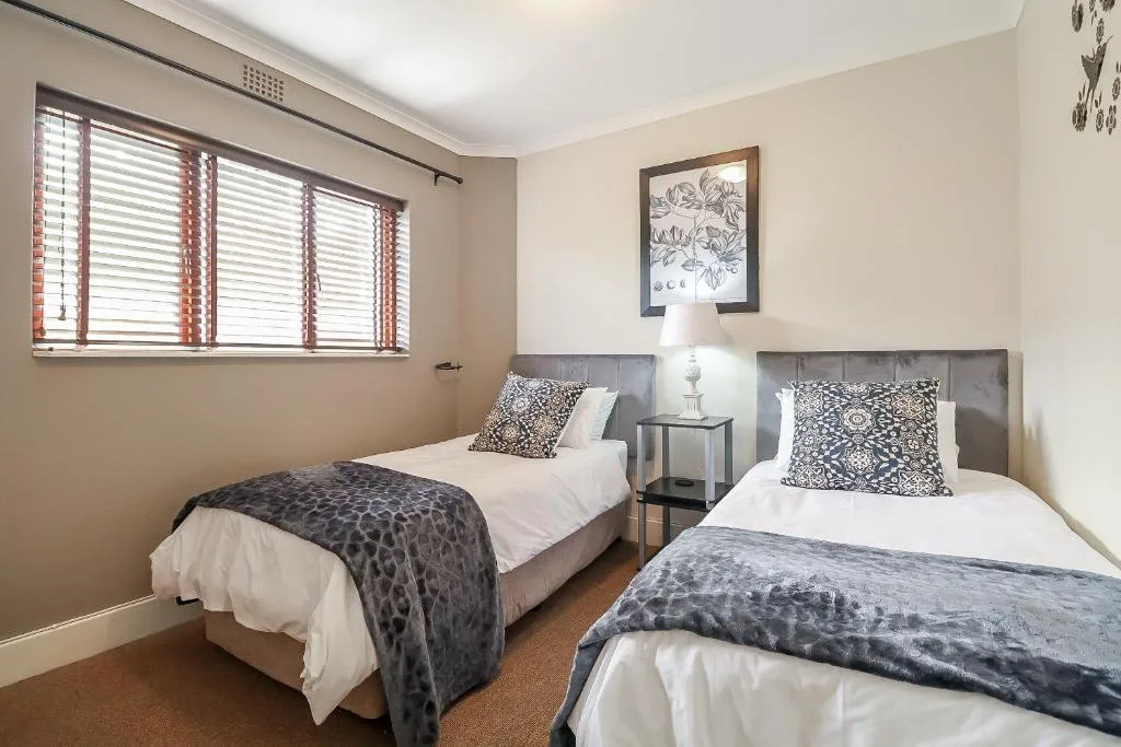 Twin bedroom with two single beds, patterned cushions, and wooden shutters