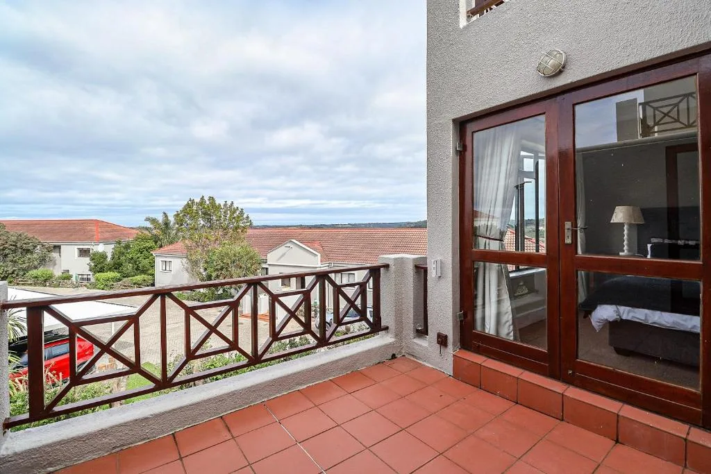 Spacious balcony with terracotta tiles and wooden railing overlooking neighborhood