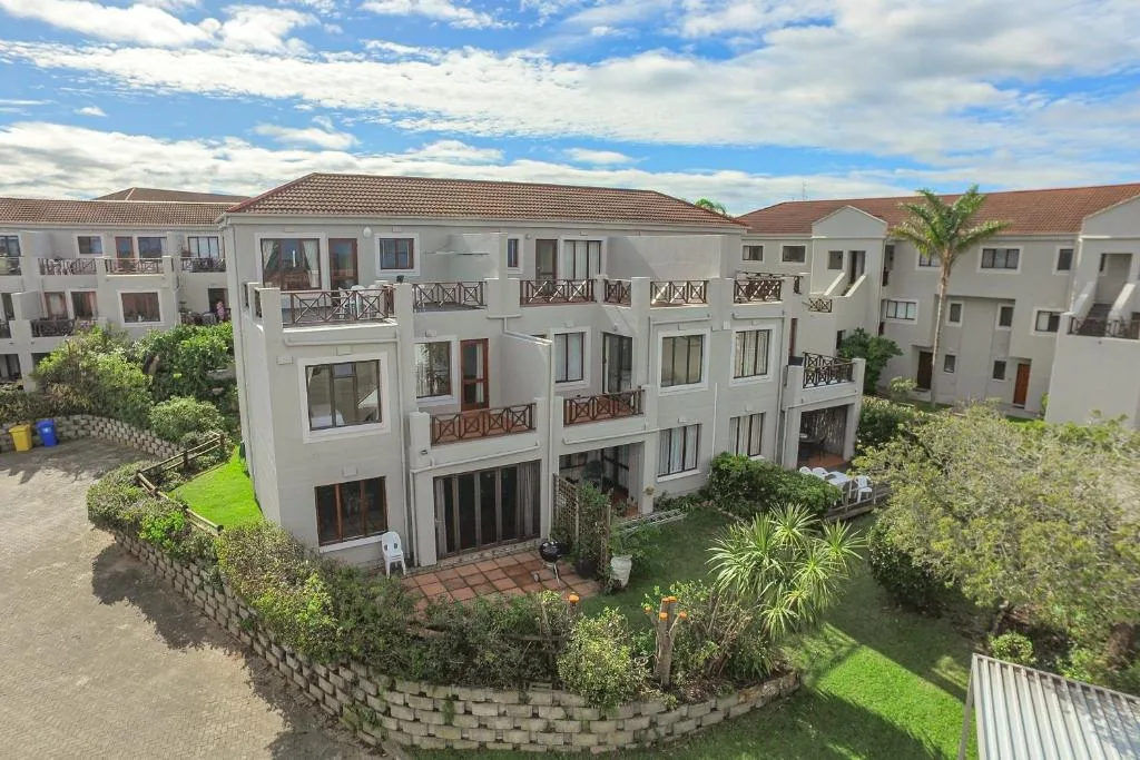 White multi-story apartment building with balconies and manicured garden surroundings