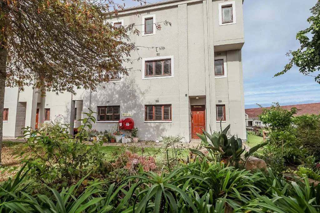 White apartment building with red door and lush garden landscaping