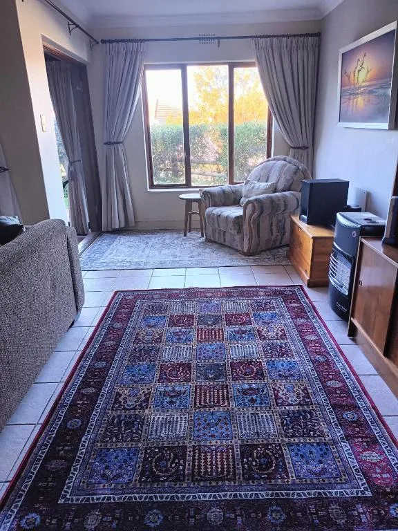 Spacious lounge with armchair, sofa, patterned rug, large windows overlooking garden