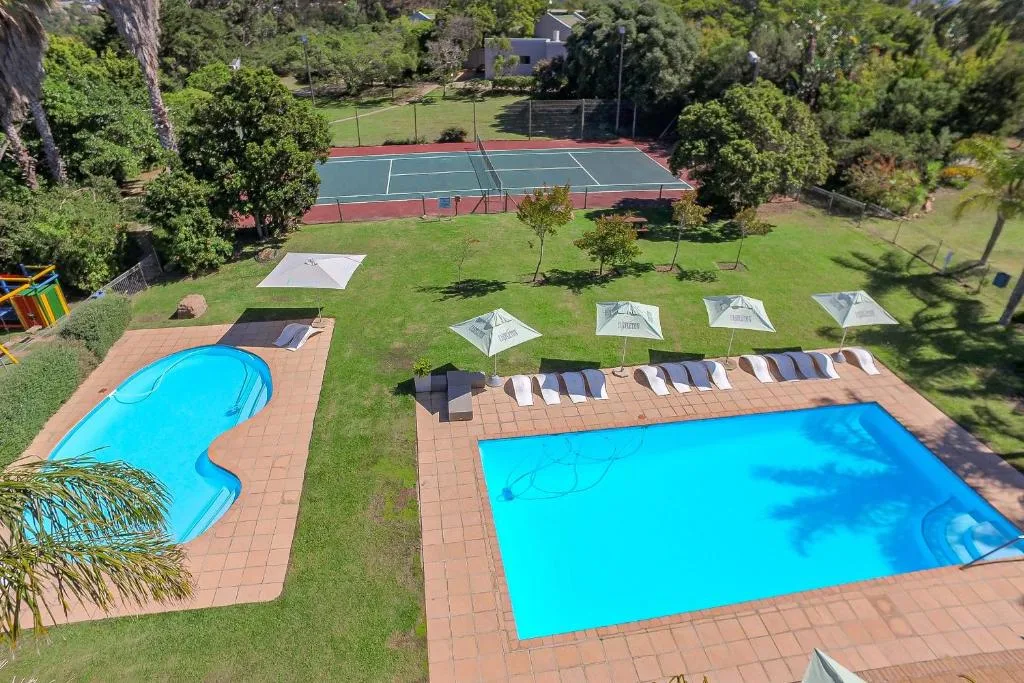 Two bright blue swimming pools with loungers and umbrellas in sunny garden setting