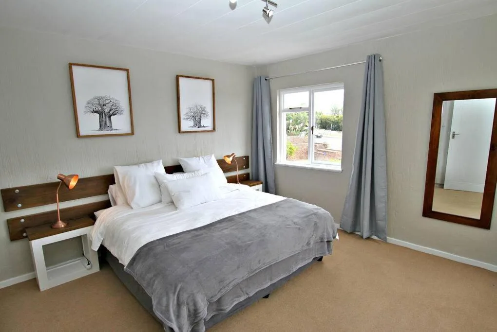 Spacious bedroom with queen bed, wooden headboard, and garden views through windows