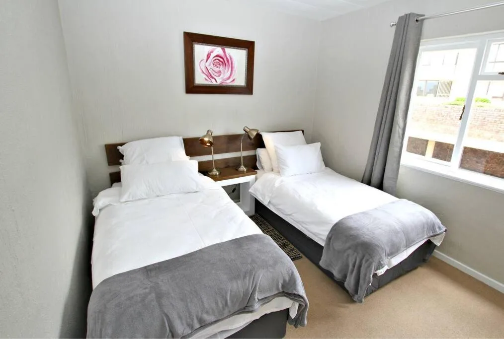 Twin bedroom with white bedding, dark headboard, and pink rose artwork on wall