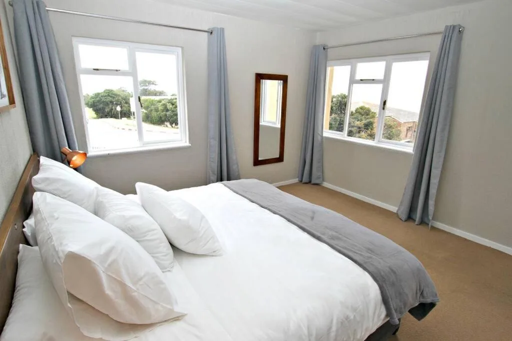 Bright bedroom with queen bed, large windows overlooking garden landscape