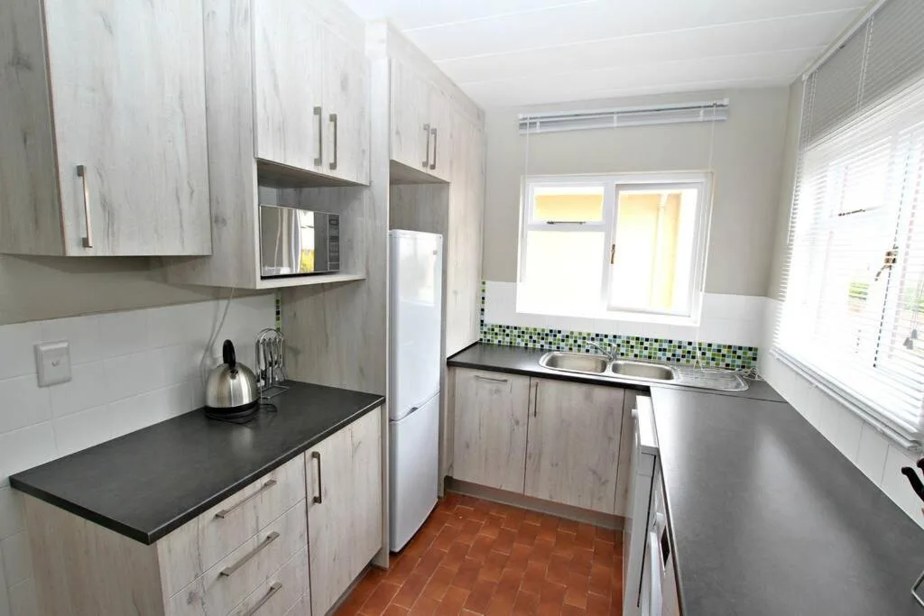 Modern kitchen with light wood cabinetry, black countertops, and tiled backsplash