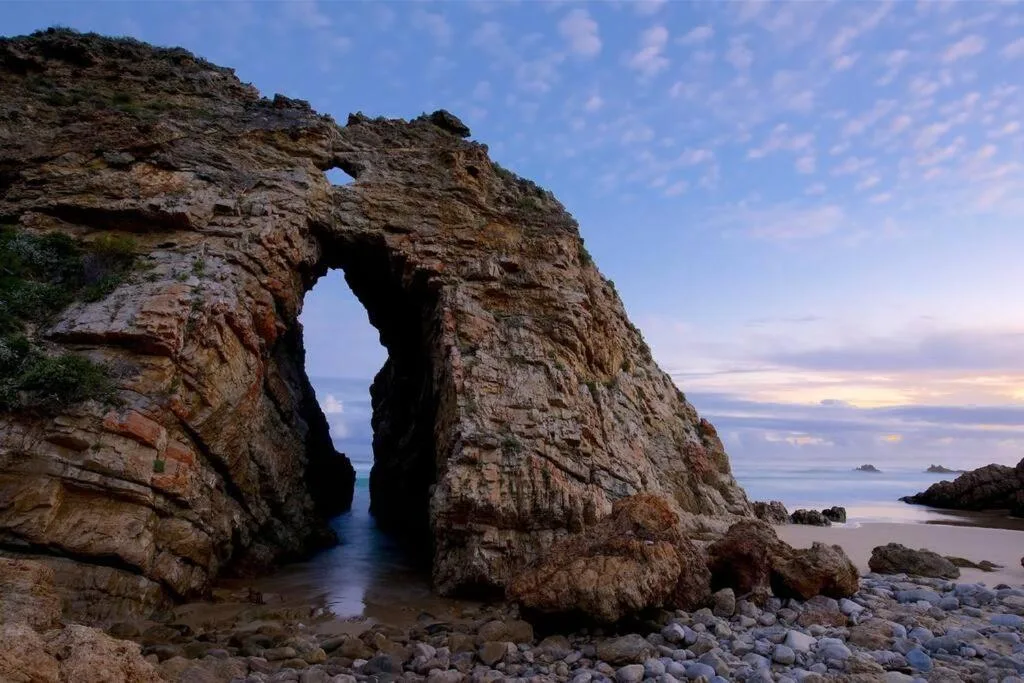 Dramatic rocky coastal archway at sunset overlooking calm ocean waters