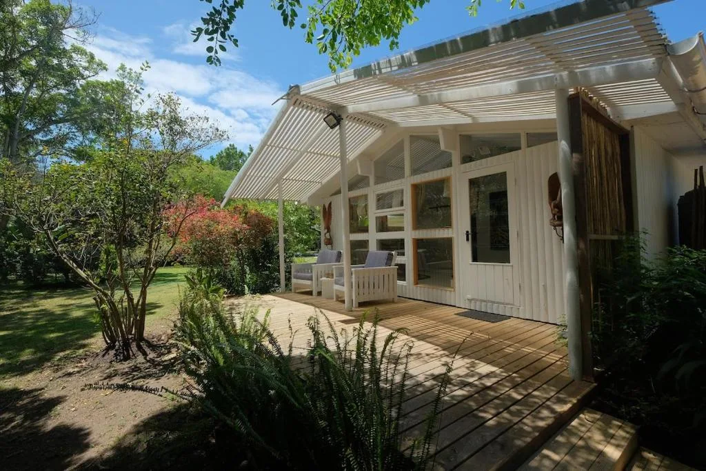 Covered wooden deck with pergola, garden seating, and surrounding greenery