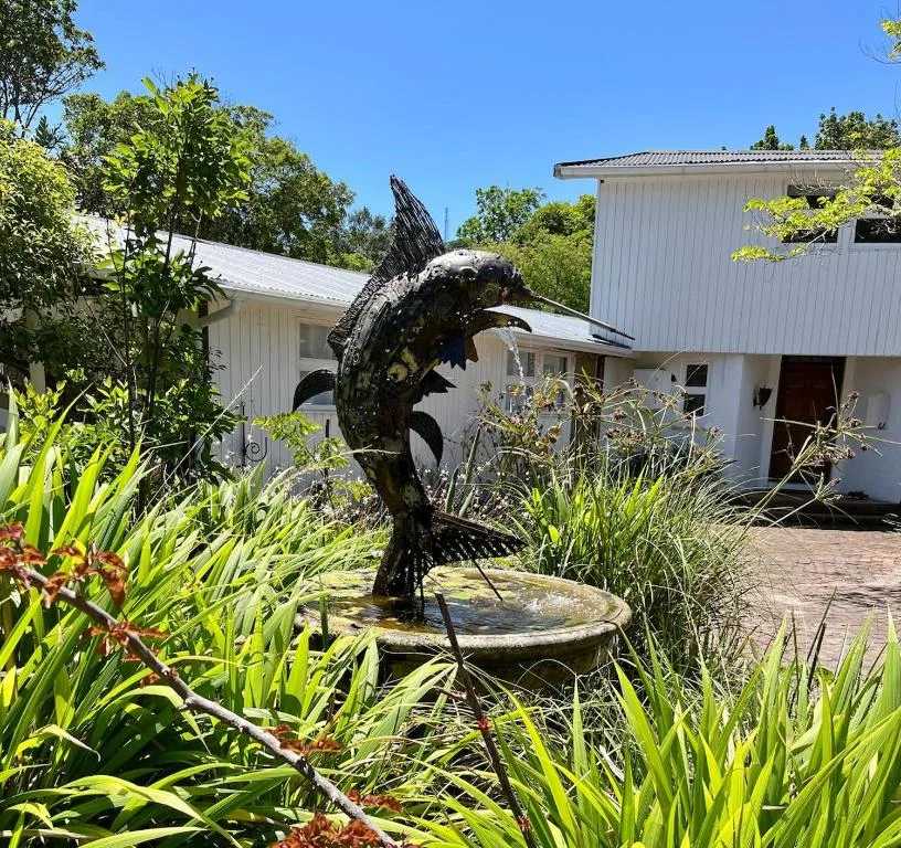 Modern white cottage with artistic fish sculpture and lush garden landscaping